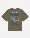 A brown short-sleeve t-shirt with a vintage-style campfire rodeo graphic printed on the back, featuring teal and tan illustrations of cowboy goats, a campfire, mountains, and text reading 'CAMPFIRE RODEO' and 'GOAT USA'.