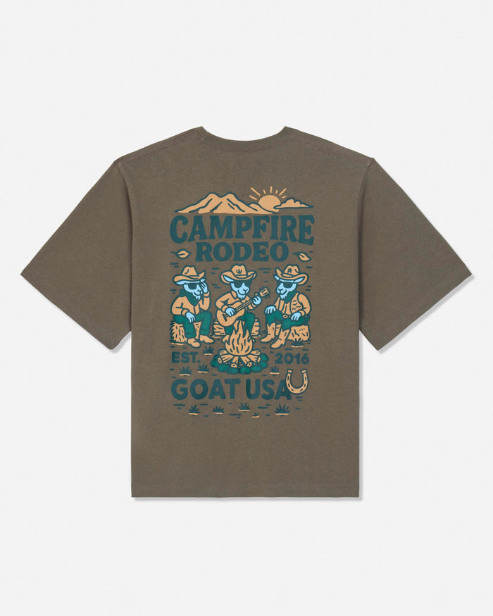 A brown short-sleeve t-shirt with a vintage-style campfire rodeo graphic printed on the back, featuring teal and tan illustrations of cowboy goats, a campfire, mountains, and text reading 'CAMPFIRE RODEO' and 'GOAT USA'.