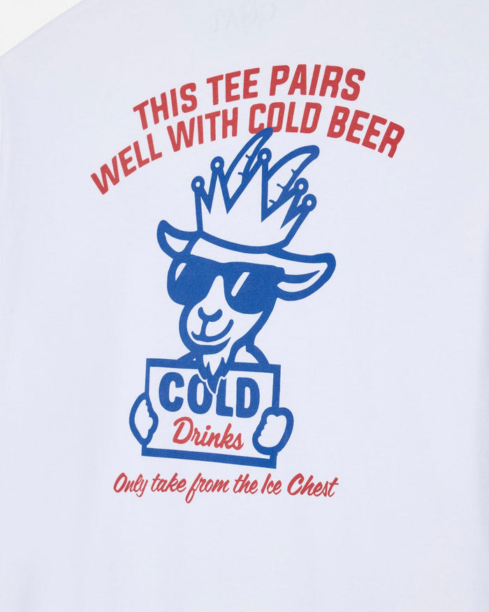A close-up of a white t-shirt featuring a blue and red graphic of a cartoon goat wearing a crown and sunglasses, holding a sign that says 'COLD Drinks'. Arched red text above reads 'THIS TEE PAIRS WELL WITH COLD BEER' and cursive red text below reads 'Only take from the Ice Chest'.