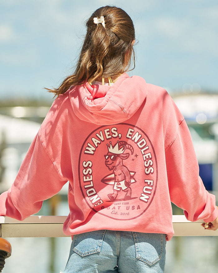 Girl in salmon-colored hoodie facing away from the camera overlooking a body of water and boats
