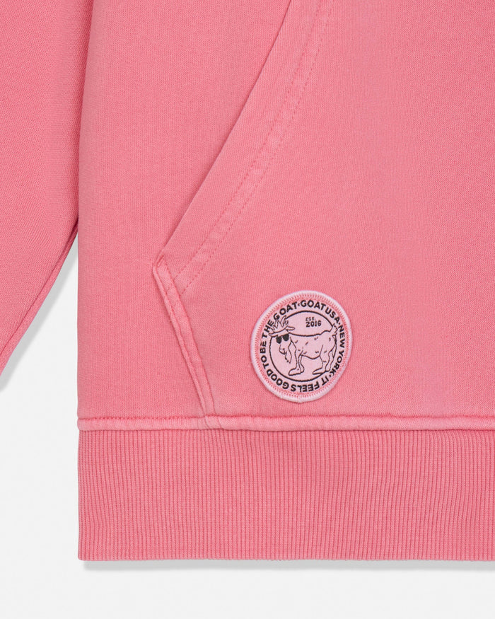 Close-up of a salmon-colored sweatshirt with a logo on the pocket against a white background