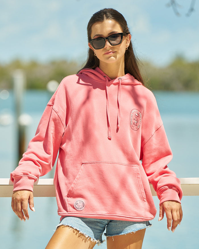 Girl in salmon-colored hoodie leaning on a ledge with a blurred water background