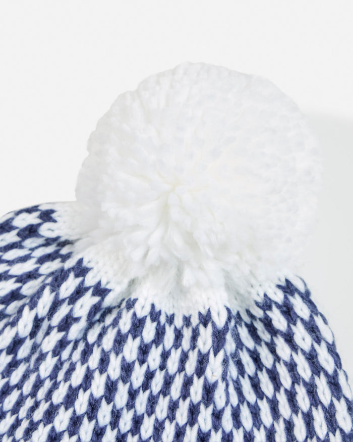 Close-up of a blue and white patterned beanie with a fluffy pom-pom on a light gray background