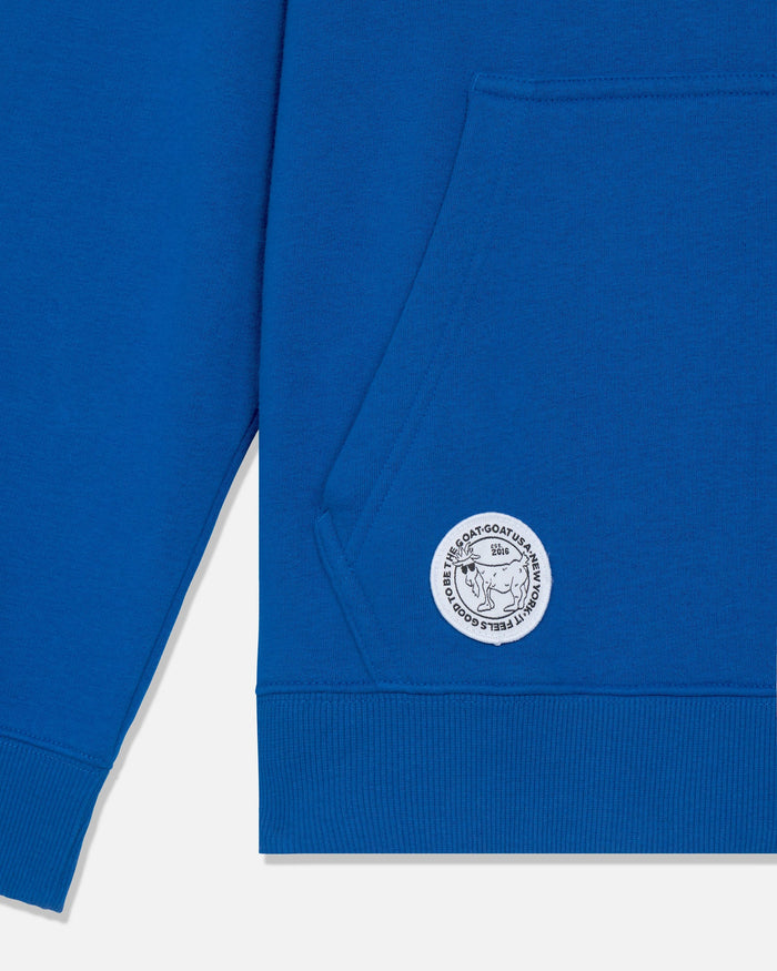 Close-up of a royal blue sweatshirt showing the left chest pocket and a circular white embroidered logo patch on the lower front.