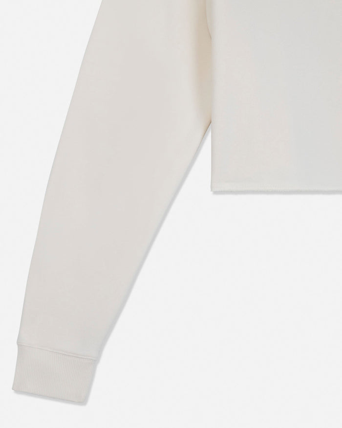 Close-up of a light cream or off-white long-sleeve garment, showing the sleeve cuff and part of the body fabric against a plain white background.