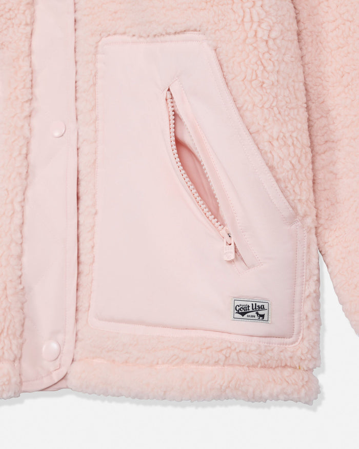 Close-up of a light pink fleece jacket showing a zippered pocket with a small rectangular brand patch reading 'GOAT USA'.