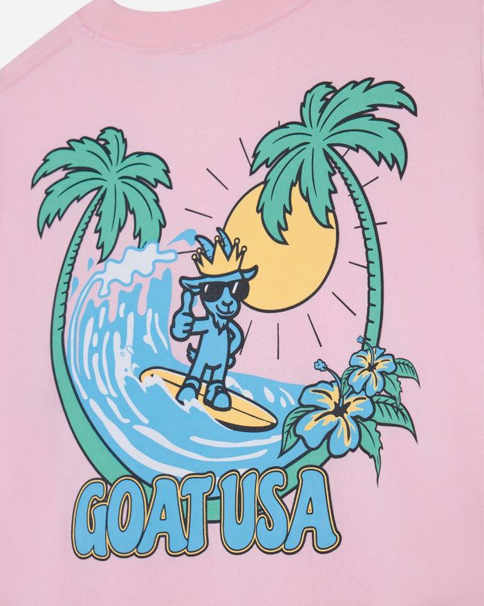 Pink t-shirt with a graphic of a character surfing, palm trees, and flowers on a pink background.