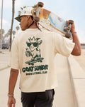 Person holding a skateboard with a graphic t-shirt featuring 'GOAT SUNDAY Brew & Stroll Club' design.