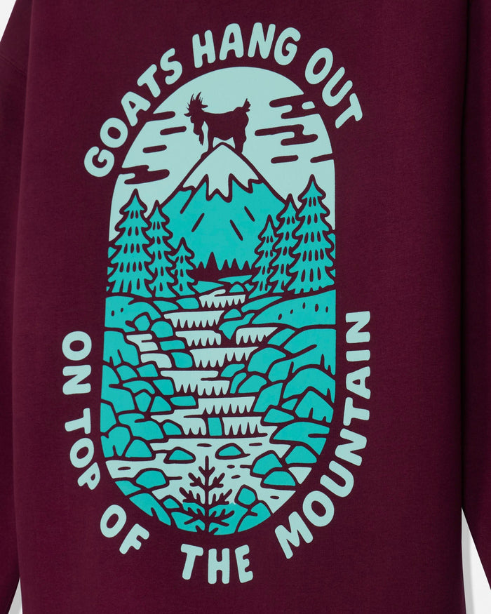 A close-up of a maroon sweatshirt featuring a large graphic print. The graphic shows a mountain, pine trees, rocks, and a goat silhouette, with the text 'GOATS HANG OUT ON TOP OF THE MOUNTAIN' in white.