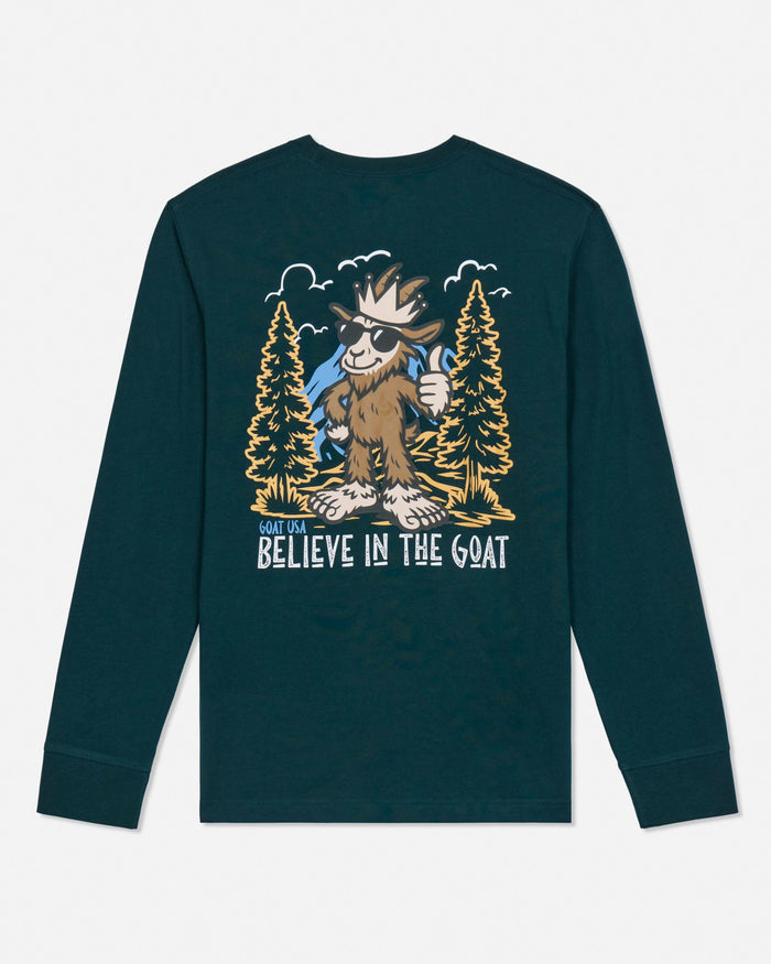 A dark teal long-sleeve t-shirt with a large graphic print on the front featuring a cartoon goat in a forest with the text 'GOAT USA BELIEVE IN THE GOAT'.