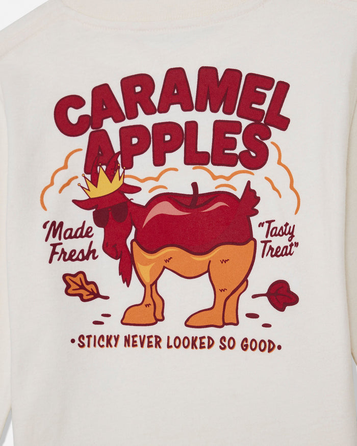 Close-up of a cream-colored garment featuring a colorful graphic print of a goat-shaped caramel apple with the text 'CARAMEL APPLES' and 'Made Fresh Tasty Treat'.