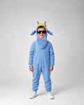 A child wearing a light blue full-body costume with a fuzzy hood, pointed ears, and a small yellow crown, standing against a plain light gray studio background.