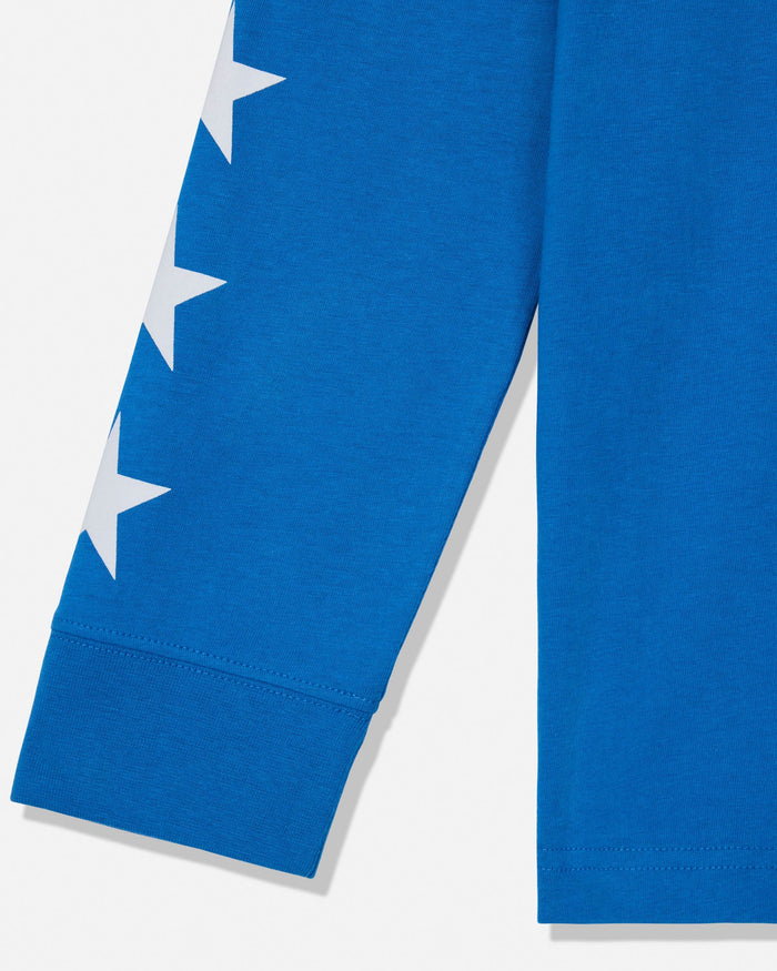Close-up of a bright blue garment sleeve with a vertical white star graphic and ribbed cuff, shown against a light neutral background.