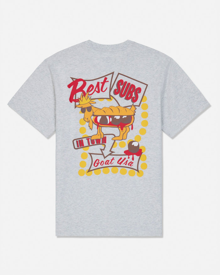 A light heather gray short-sleeve t-shirt with a retro-style graphic on the front. The graphic features a cartoon pie character wearing sunglasses and holding a sign that says 'Best SUBS', with 'Goat USA' written below in red script, surrounded by yellow polka dots.