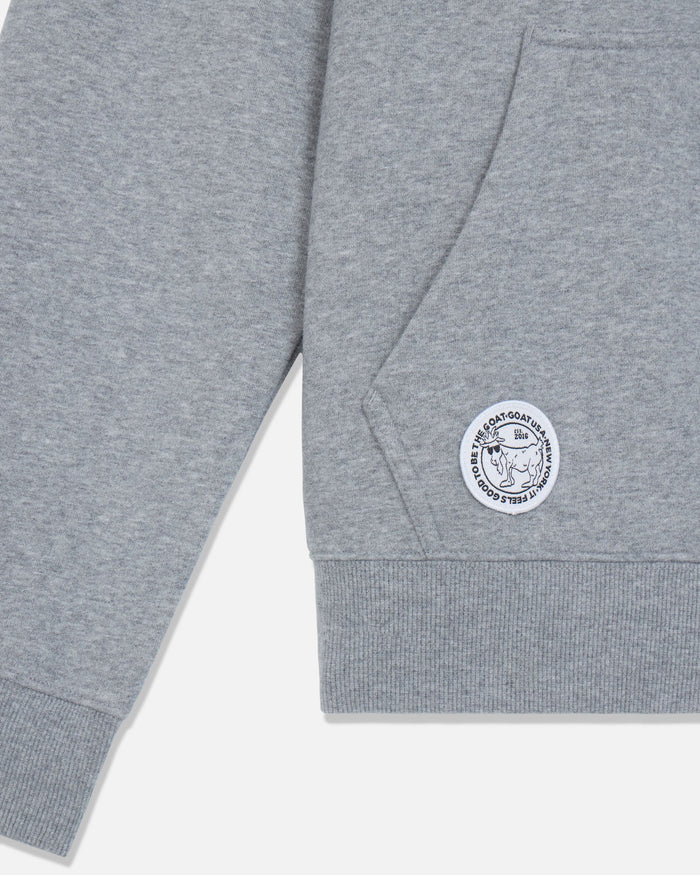 Close-up of a heather gray sweatshirt sleeve with a ribbed cuff and a circular white embroidered patch featuring a goat.