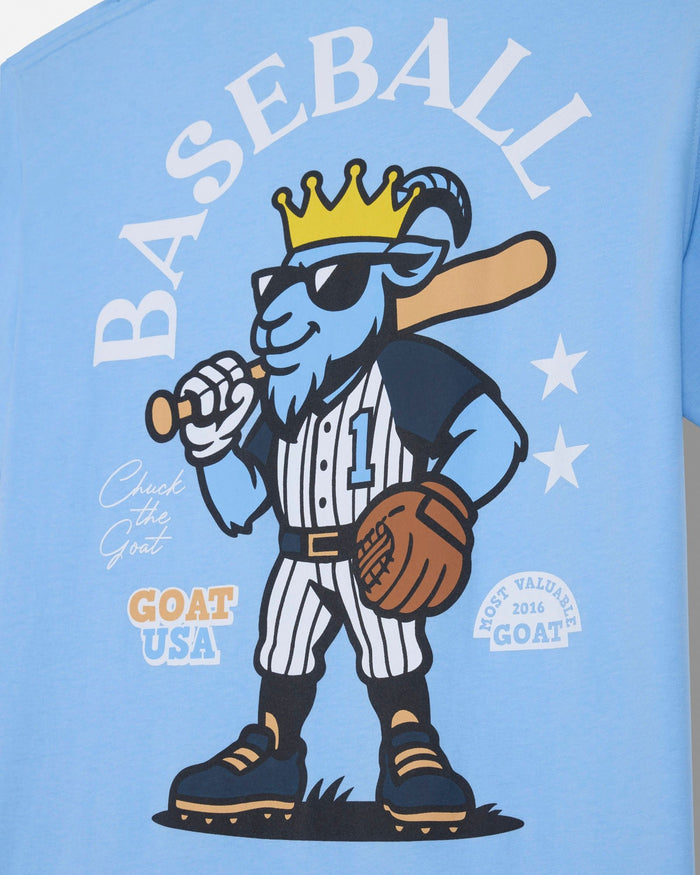 A close-up of a light blue t-shirt featuring a cartoon graphic of a blue goat baseball player wearing a gold crown and sunglasses, with the word 'BASEBALL' printed above in white.