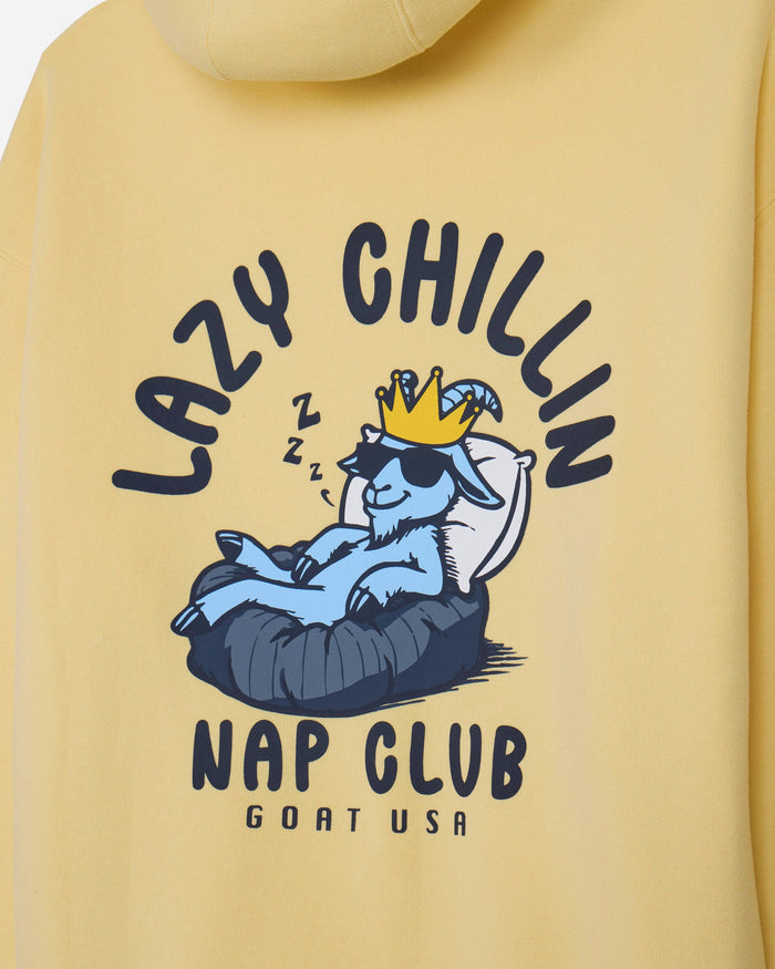 Close-up of a yellow hoodie featuring a cartoon graphic of a blue goat wearing sunglasses and a gold crown, lying in a black  bed with the text 'LAZY CHILLIN' and 'NAP CLUB GOAT USA'.