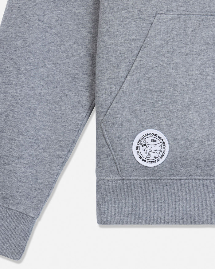 Close-up of a heather gray sweatshirt sleeve and hem, featuring a circular white embroidered patch with a goat illustration.#color_gray-heather