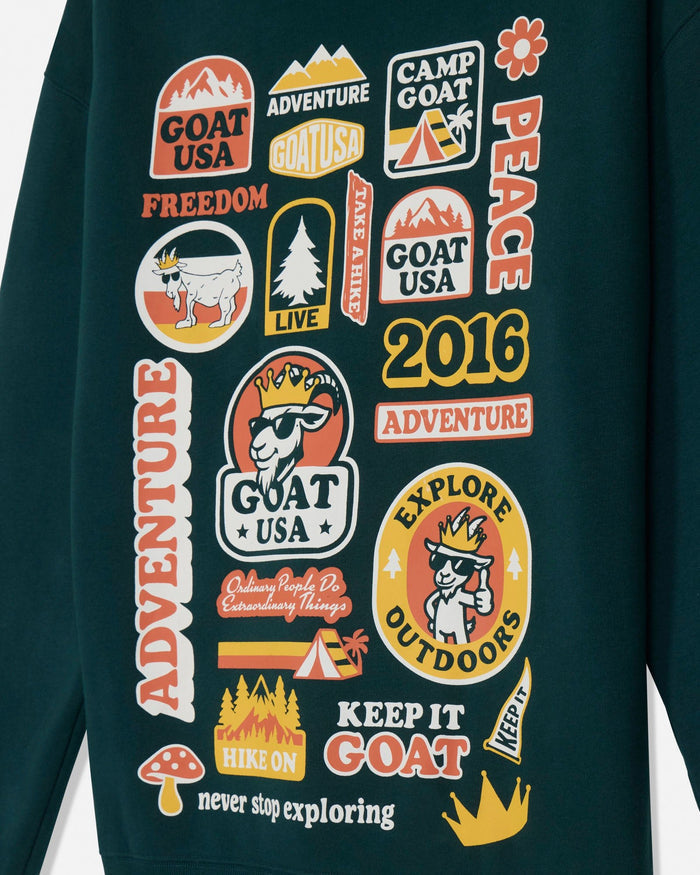 A close-up of a dark teal sweatshirt featuring a collection of colorful retro-style 'Goat USA' and outdoor-themed patches printed across the chest.