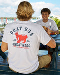 Man in white t-shirt with red lobster goat design eating at a picnic table