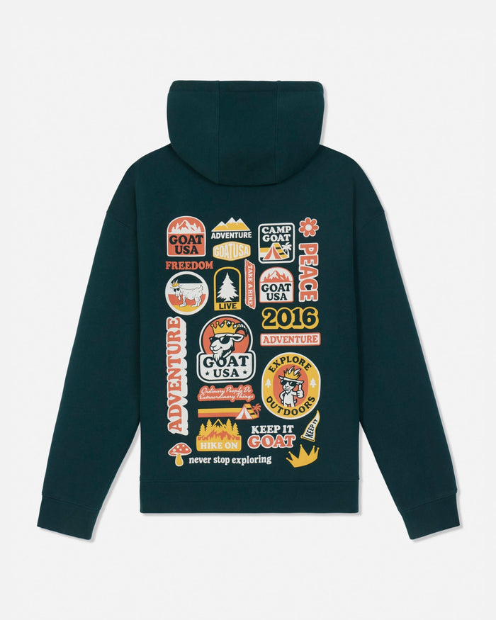A dark teal-green hooded sweatshirt shown from the back, featuring a large collage of colorful 'Goat USA Adventure' patches and graphics printed across the back.