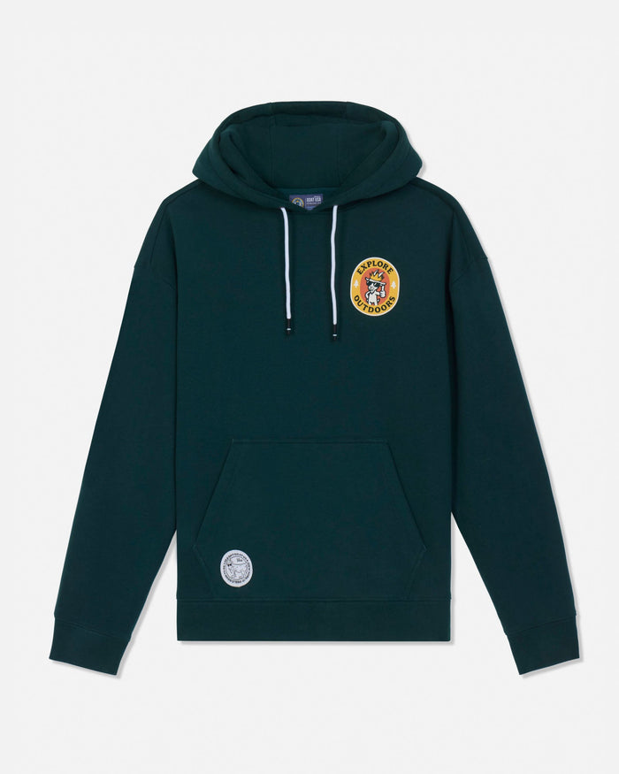 A dark green pullover hoodie with white drawstrings, featuring a circular yellow and red crest patch on the left chest and a smaller circular patch on the lower left front pocket, displayed against a light gray background.