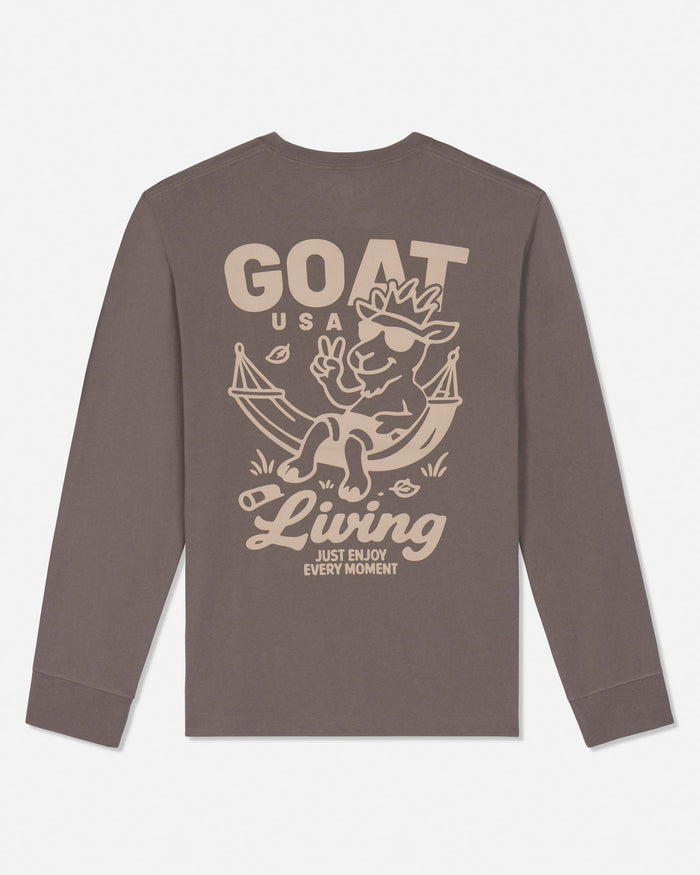 A long-sleeve crewneck t-shirt in a muted brownish-gray color, featuring a large beige graphic print on the back with a cartoon goat in a hammock and the text 'GOAT USA Living JUST ENJOY EVERY MOMENT'.