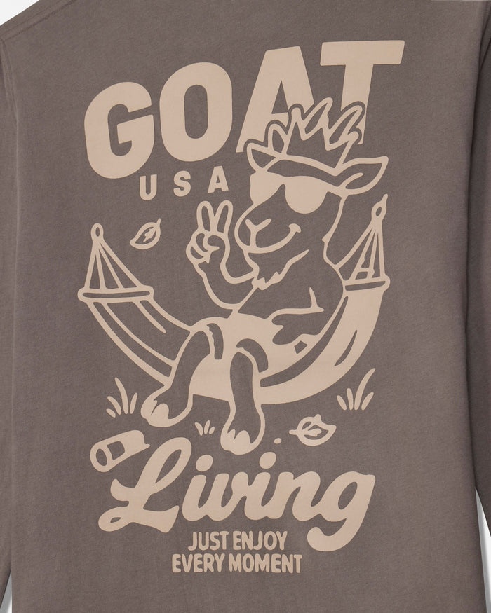 Close-up of a brown long-sleeve shirt with a beige graphic print featuring a goat lounging in a hammock with the text 'GOAT USA Living JUST ENJOY EVERY MOMENT'.