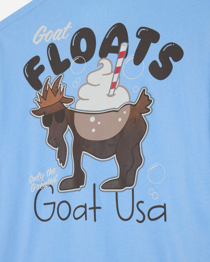 A close-up of a light blue t-shirt featuring a cartoon graphic of a brown goat wearing sunglasses and a small hat, drinking a whipped cream beverage with a red-and-white striped straw. The text 'GOAT FLOATS' is printed above the graphic, and 'Only the Greatest Goat USA' is printed below.