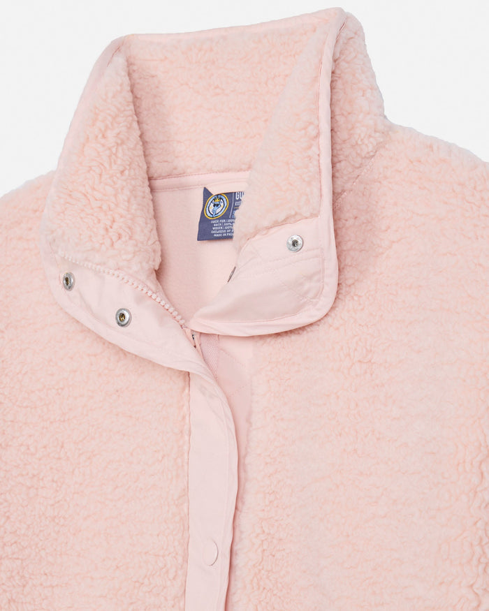 Close-up of a light pink sherpa fleece jacket with a buttoned collar and silver snap buttons, showing a small interior brand tag.