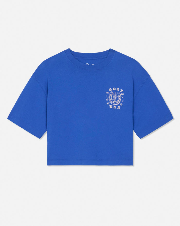 A royal blue short-sleeve crop top t-shirt with a white graphic print on the left chest featuring a horseshoe and the text 'GOAT USA'.