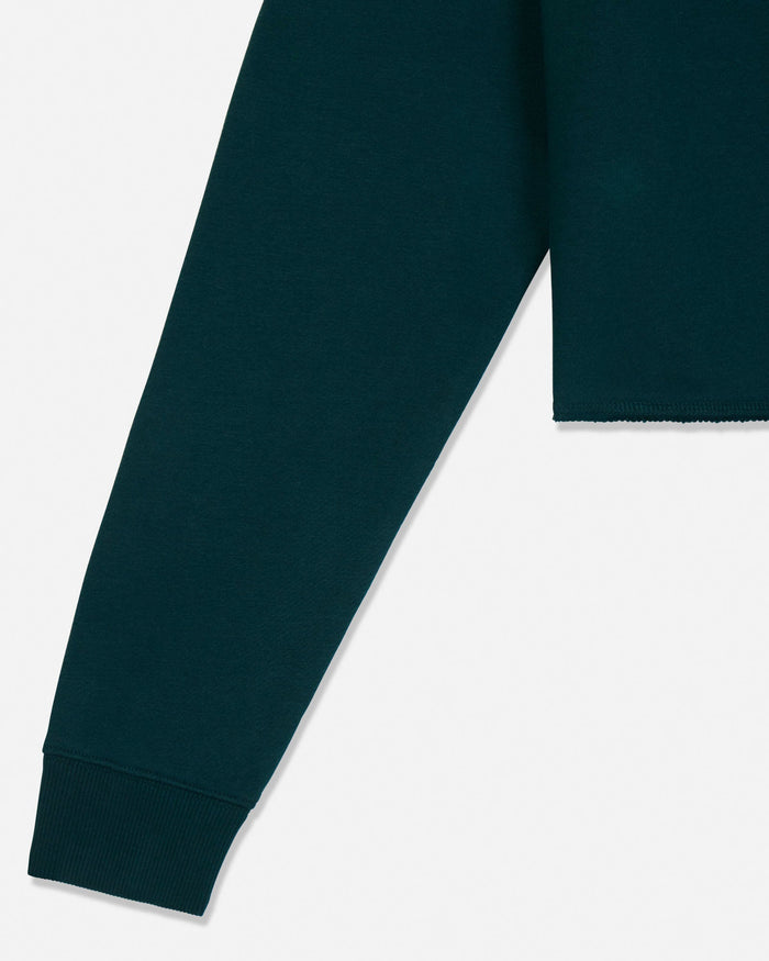 Close-up of a dark teal green sweatshirt showing the ribbed cuff and part of the sleeve against a light gray background.